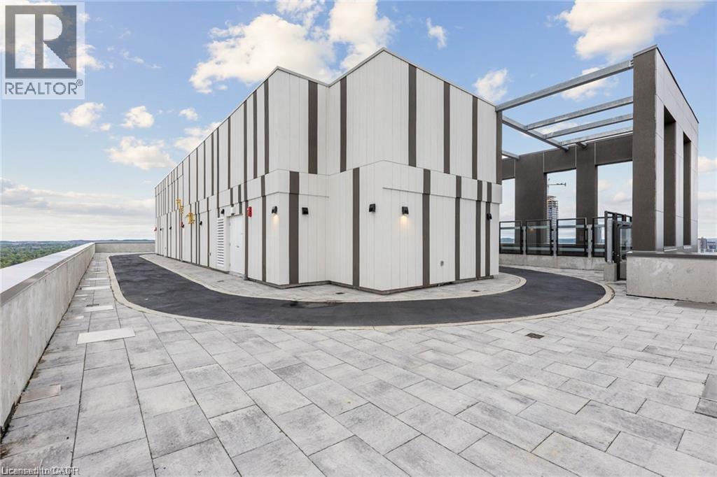 Rooftop terrace featuring light-toned paver flooring, a dark asphalt path, and a concrete perimeter wall - 85 Duke Street W Unit# 507, Kitchener, ON - Outdoor