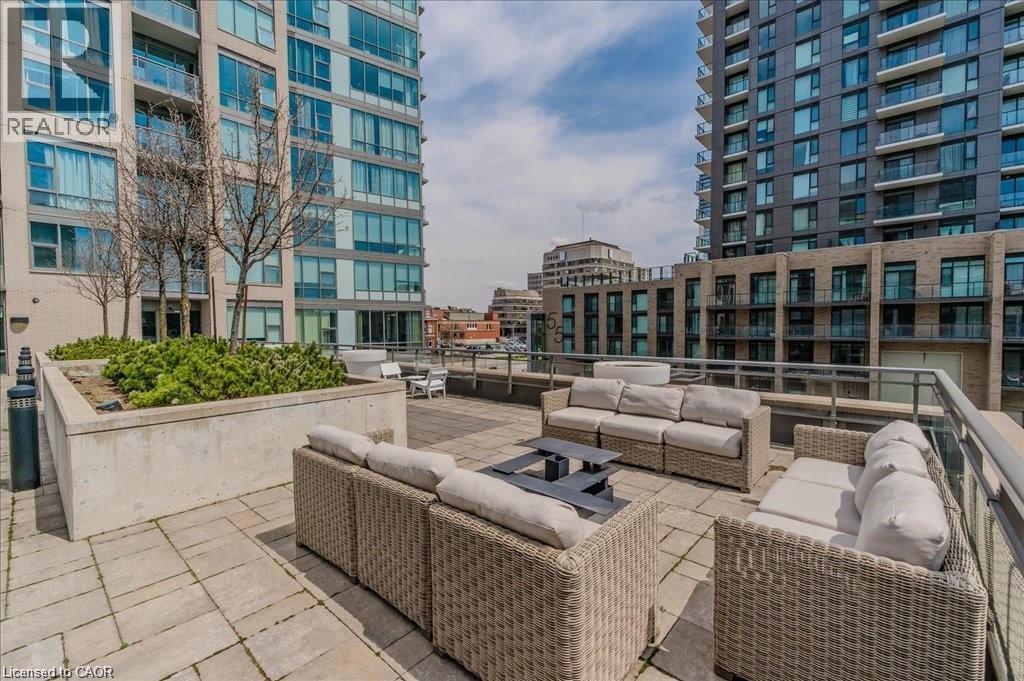 Expansive outdoor terrace featuring paver flooring, a perimeter railing, and concrete planters with mature greenery - 85 Duke Street W Unit# 507, Kitchener, ON - Outdoor With Facade