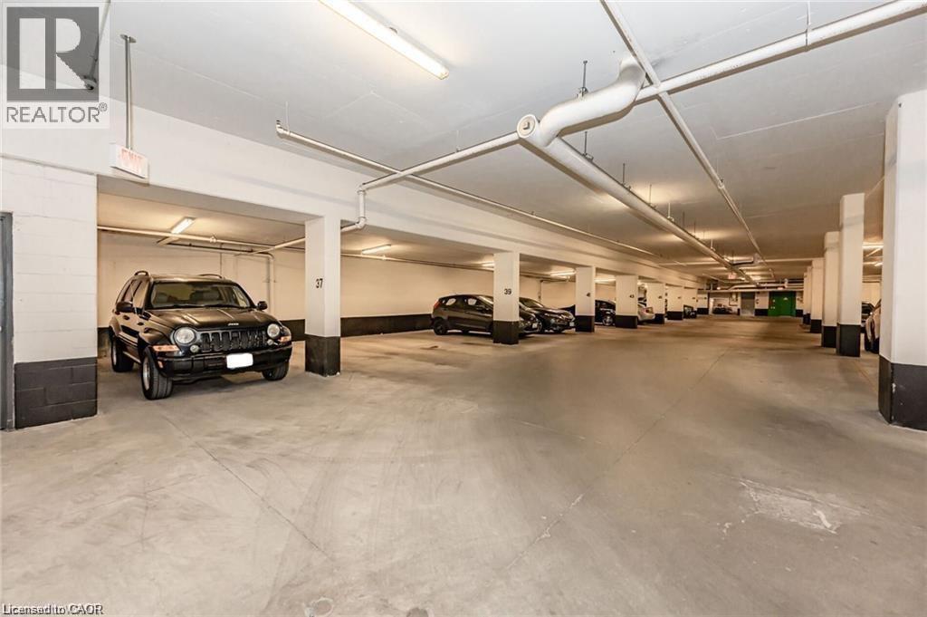 Spacious underground parking garage with concrete flooring, multiple support columns, and overhead fluorescent lighting - 85 Duke Street W Unit# 507, Kitchener, ON - Indoor Photo Showing Garage