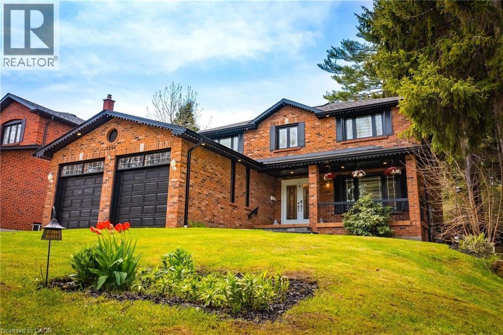 Brick exterior residence featuring a two-car garage with black paneled doors, a covered front porch with dark railings, and a white entry door with glass inserts - 1264 Kane Road, Mississauga, ON - Outdoor With Deck Patio Veranda