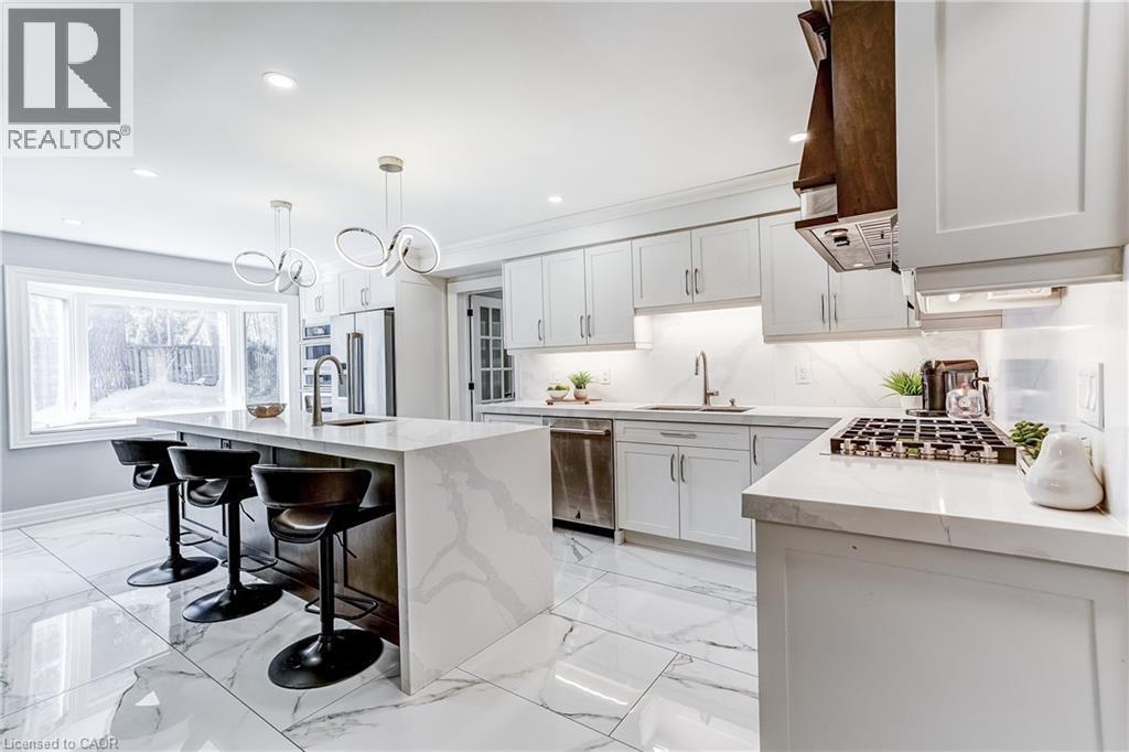 Spacious kitchen featuring white cabinetry, a large center island with integrated seating, and a gas range with a wood-finish range hood - 1264 Kane Road, Mississauga, ON - Indoor Photo Showing Kitchen With Upgraded Kitchen