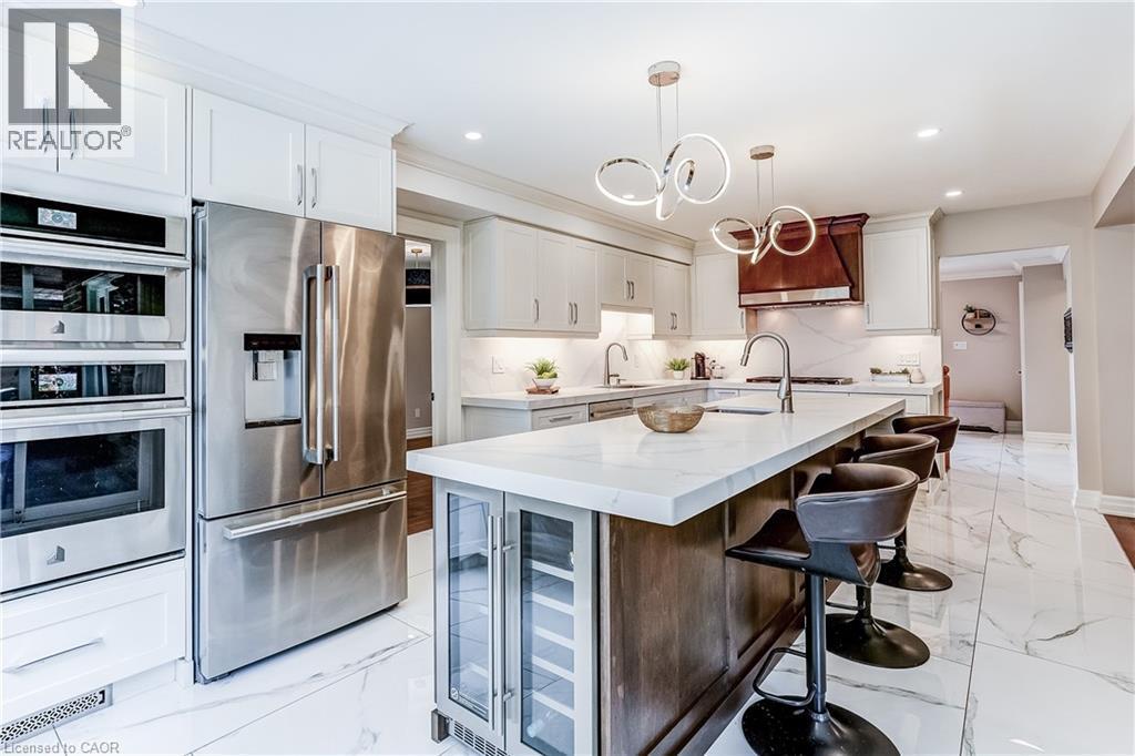 Kitchen featuring a large island with white countertop, recessed lighting, and stainless steel appliances including a built-in double oven, refrigerator, and beverage cooler - 1264 Kane Road, Mississauga, ON - Indoor Photo Showing Kitchen With Upgraded Kitchen