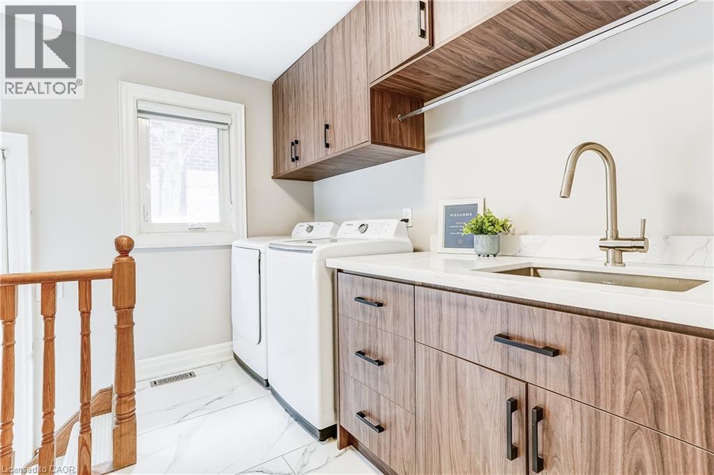 Laundry area featuring wood-finish cabinetry, a white countertop, and a stainless steel sink with a gooseneck faucet - 1264 Kane Road, Mississauga, ON - Indoor Photo Showing Laundry Room