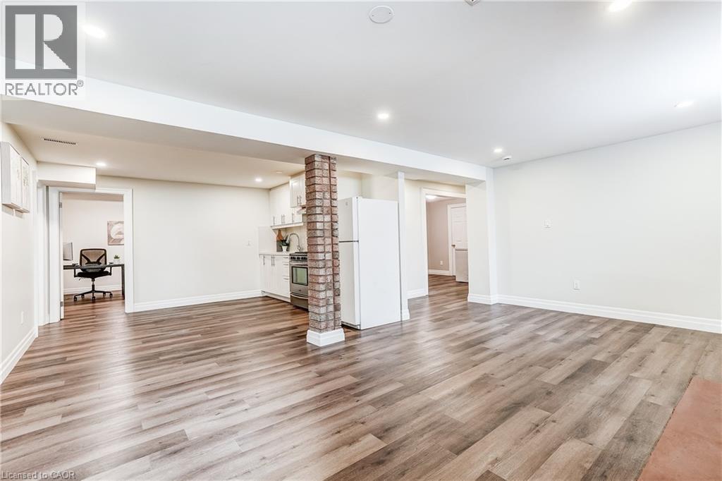 Open-concept living space featuring wood-finish flooring, recessed lighting, and a partial kitchen with white cabinetry and a full-size refrigerator - 1264 Kane Road, Mississauga, ON - Indoor