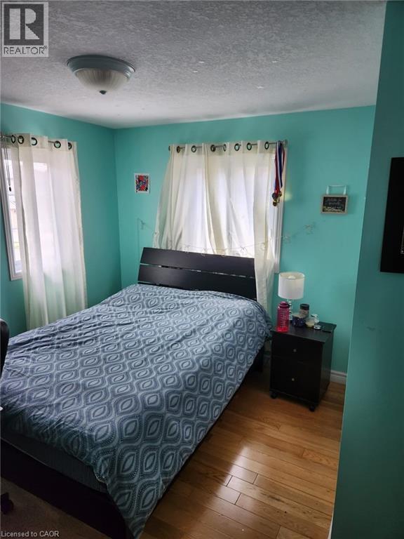 Bedroom featuring wood-finish flooring and two windows with white sheer curtains - 1126 Copper Leaf Crescent, Kitchener, ON - Indoor Photo Showing Bedroom