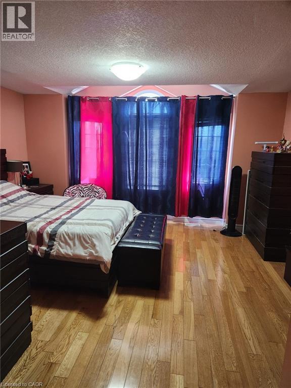 Spacious room featuring wood-finish flooring, a contemporary ceiling light fixture, and a window arrangement with an arched transom - 1126 Copper Leaf Crescent, Kitchener, ON - Indoor Photo Showing Bedroom