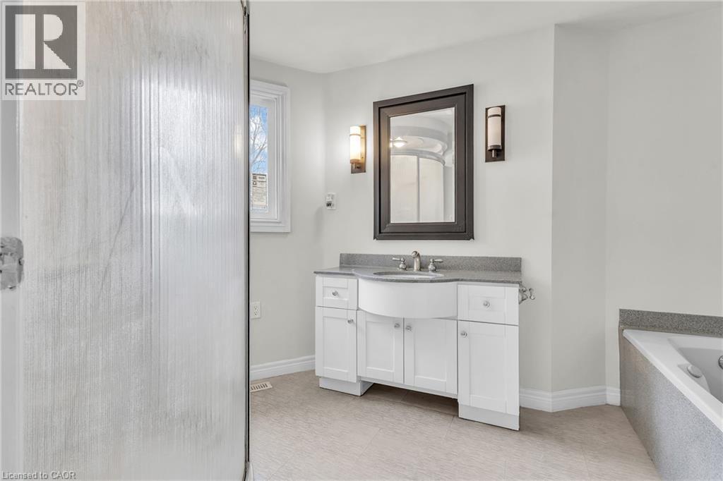 Bathroom vanity with a curved sink, stone countertop, white cabinetry, and wall-mounted sconces - 22 Blackhorne Crescent, Kitchener, ON - Indoor Photo Showing Bathroom