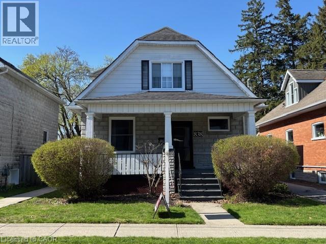 Charming dormer-style residence featuring a covered front porch with white pillars, a stone facade, and horizontal siding - 838 Moore Street, Cambridge, ON - Outdoor With Deck Patio Veranda