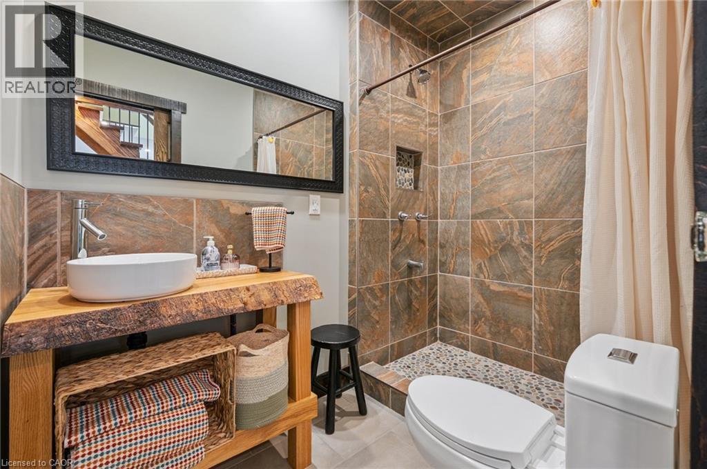 Bathroom featuring a live-edge wood vanity with a vessel sink, a full-length framed mirror, and a tiled shower with a pebble floor - 838 Moore Street, Cambridge, ON - Indoor Photo Showing Bathroom