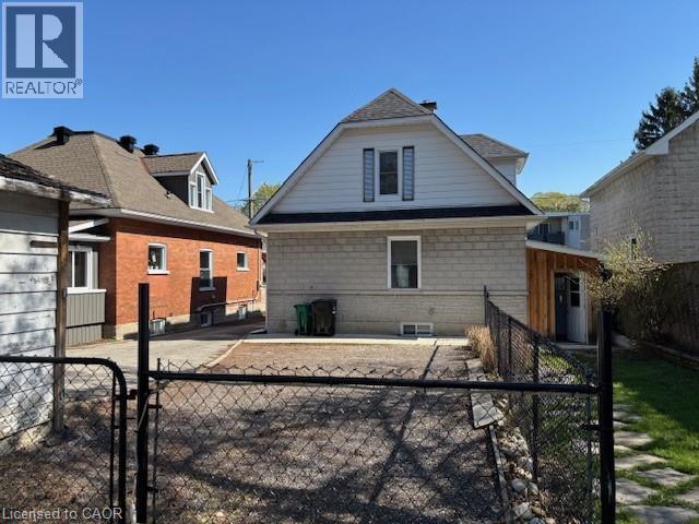 Rear exterior featuring a light-colored brick facade, white siding on the upper level, a dark shingled roof, a ground-level window, and a small, fenced yard - 838 Moore Street, Cambridge, ON - Outdoor