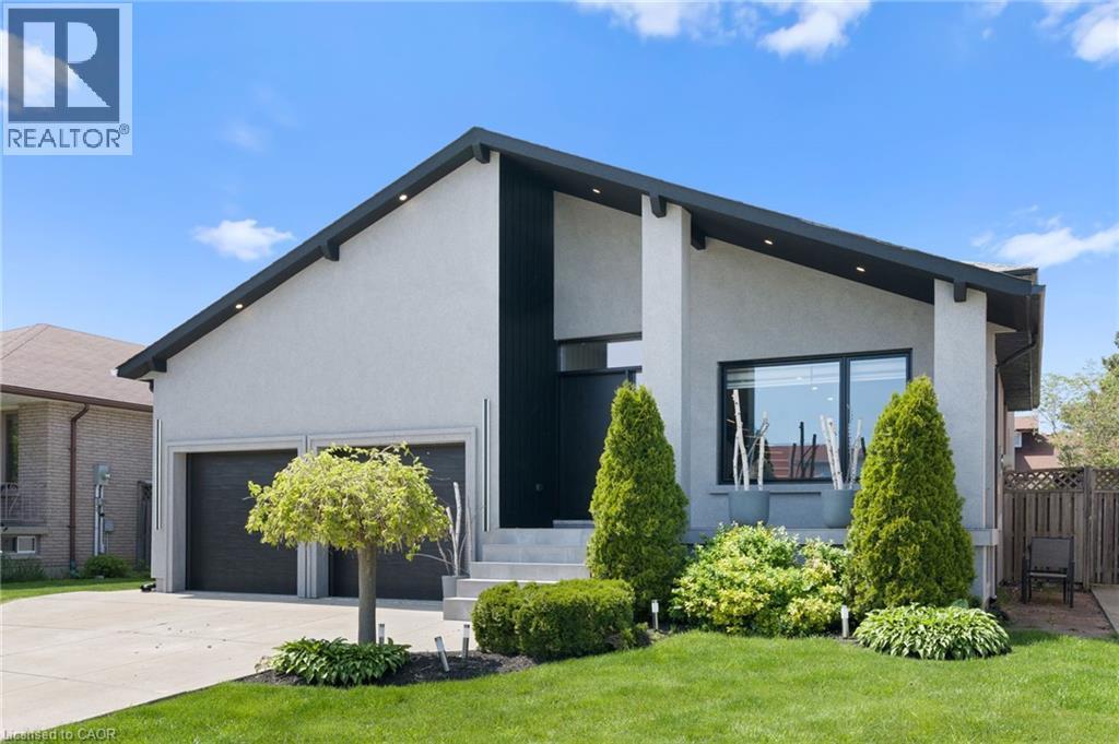 Modern facade featuring a prominent black vertical accent, expansive driveway, two-car garage, manicured lawn, and mature landscaping - 17 Clearview Drive, Hamilton, ON - Outdoor