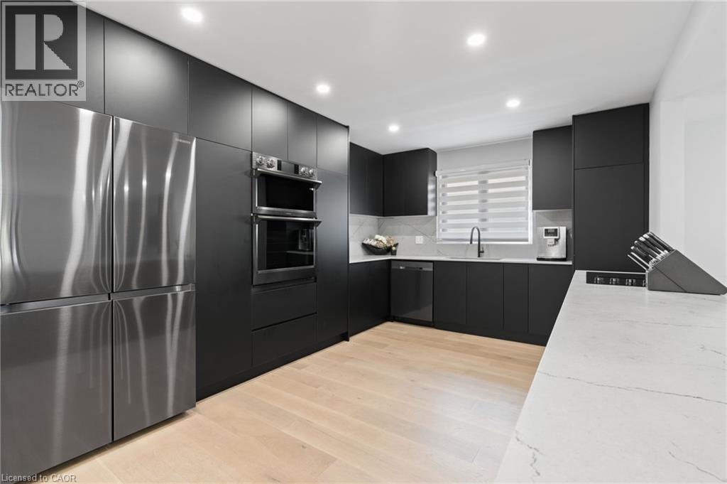 Kitchen featuring dark cabinets, appliances with stainless steel finishes, modern cabinets, light wood finished floors, and tasteful backsplash - 17 Clearview Drive, Hamilton, ON - Indoor Photo Showing Kitchen