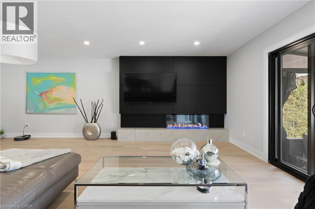 Modern living area featuring a black built-in media console with integrated electric fireplace, light wood-finish flooring, recessed ceiling lighting, and a white drum pendant light - 17 Clearview Drive, Hamilton, ON - Indoor Photo Showing Living Room