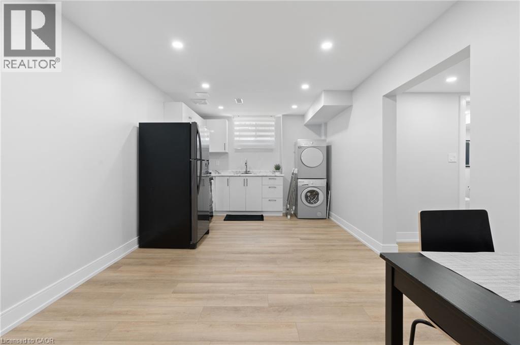 Kitchen with freestanding refrigerator, stacked washing machine and dryer, white cabinetry, light countertops, and light wood-type flooring - 17 Clearview Drive, Hamilton, ON - Indoor Photo Showing Laundry Room