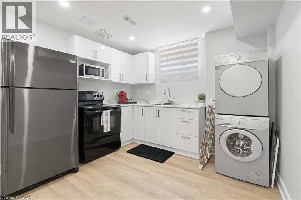 Kitchen with stainless steel appliances, white cabinetry, stacked washer / dryer, light wood-style floors, and modern cabinets - 17 Clearview Drive, Hamilton, ON - Indoor Photo Showing Laundry Room