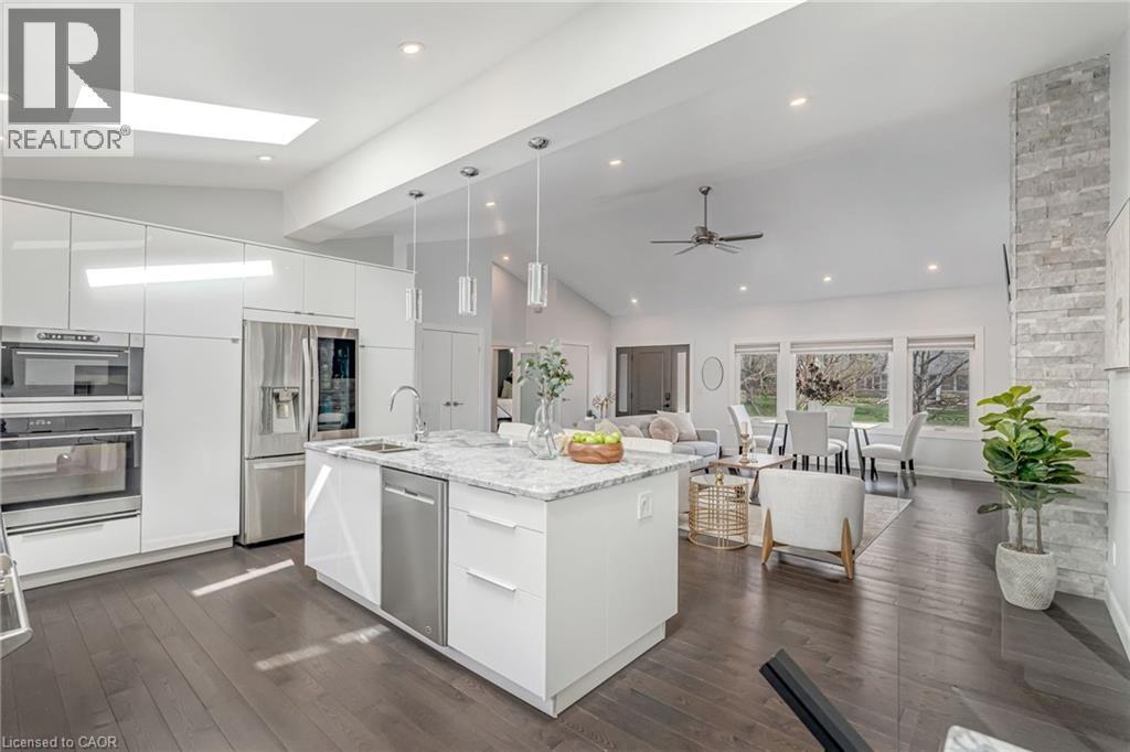 Open-concept living area with vaulted ceilings, dark wood-finish flooring, and a kitchen featuring a large central island with a sink, white cabinetry, and stainless steel appliances - 2123 Deyncourt Drive, Burlington, ON - Indoor Photo Showing Kitchen With Upgraded Kitchen