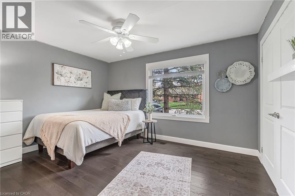 Spacious room featuring dark wood-finish flooring, a large window with white trim, and a ceiling fan with integrated lighting - 2123 Deyncourt Drive, Burlington, ON - Indoor Photo Showing Bedroom