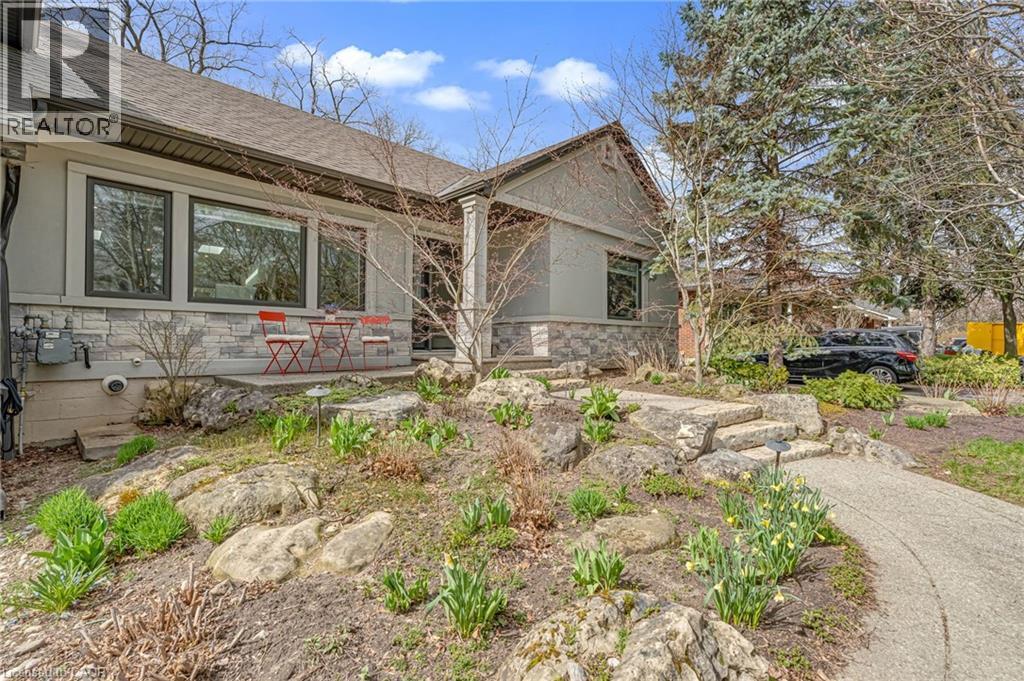 Ranch-style residence featuring a prominent stone facade, a covered porch entry, large picture windows, and a paved driveway - 2123 Deyncourt Drive, Burlington, ON - Outdoor
