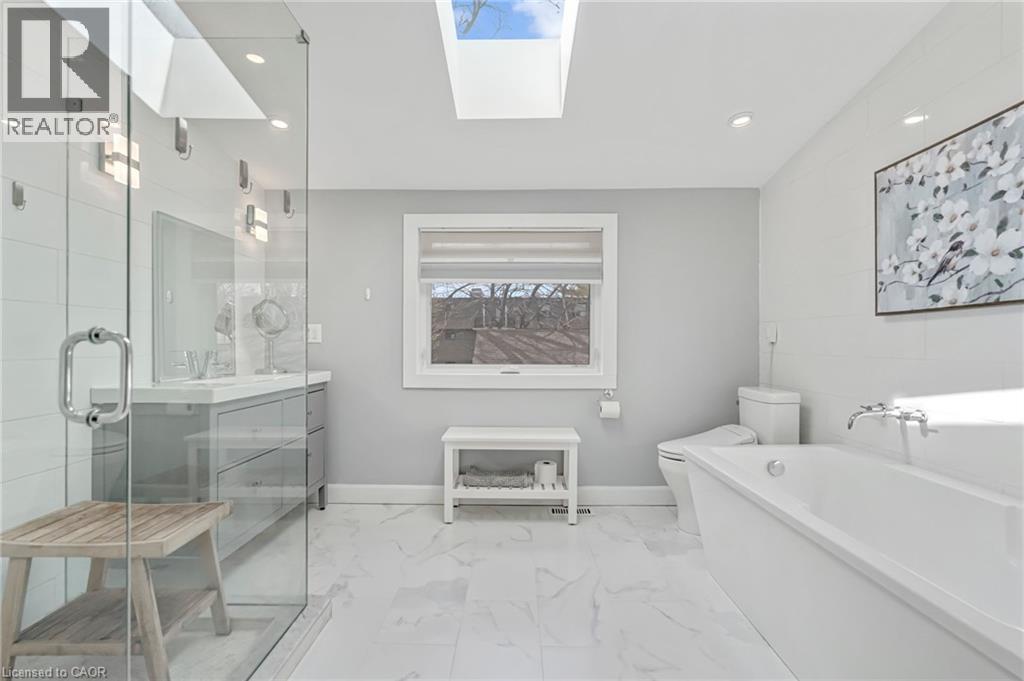 Contemporary bathroom featuring a freestanding tub, glass-enclosed shower, dual vanity with undermount sinks, skylights, and large format marble-look floor tiles - 2123 Deyncourt Drive, Burlington, ON - Indoor Photo Showing Bathroom