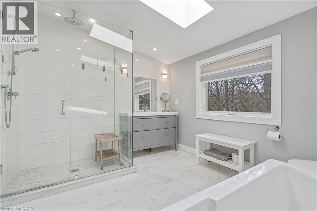 Contemporary bathroom featuring a glass-enclosed shower with a rainfall showerhead, a large soaking tub, a vanity with ample storage, and a skylight - 2123 Deyncourt Drive, Burlington, ON - Indoor Photo Showing Bathroom