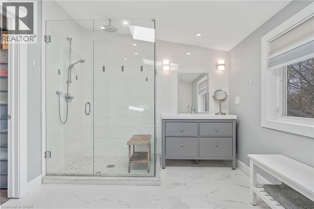 Spacious bathroom featuring a glass-enclosed shower with multiple showerheads, a skylight, and white subway tile - 2123 Deyncourt Drive, Burlington, ON - Indoor Photo Showing Bathroom