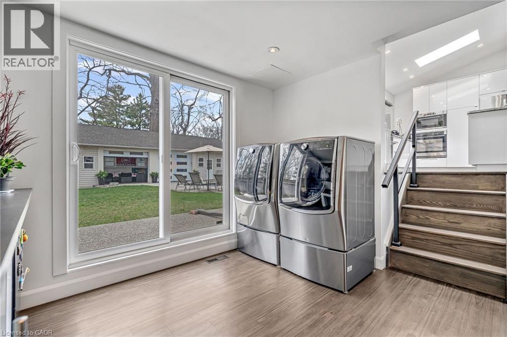 Spacious utility area featuring wood-finish flooring, a large sliding glass door, and a built-in staircase with a dark wood finish and black metal railing - 2123 Deyncourt Drive, Burlington, ON - Indoor Photo Showing Laundry Room