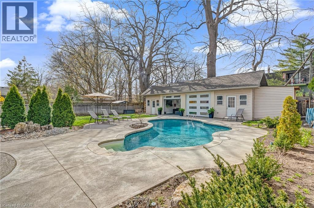 Freeform swimming pool with integrated spa, surrounded by extensive concrete decking - 2123 Deyncourt Drive, Burlington, ON - Outdoor With In Ground Pool