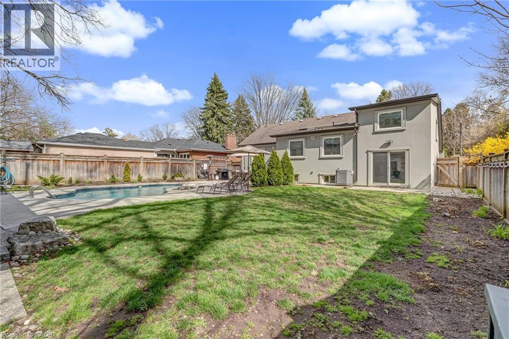 Rear yard featuring a swimming pool with concrete decking, a stucco exterior, and a wood fence enclosure - 2123 Deyncourt Drive, Burlington, ON - Outdoor With In Ground Pool