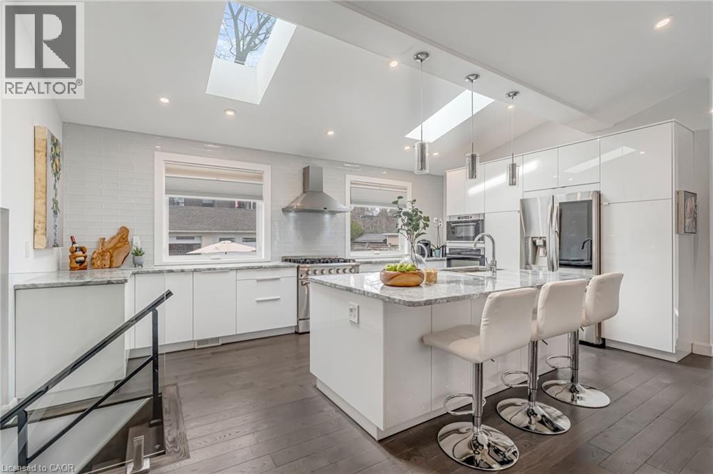 Bright kitchen featuring wood-finish flooring, white cabinetry, integrated stainless steel appliances, a center island with countertop seating, and multiple skylights - 2123 Deyncourt Drive, Burlington, ON - Indoor Photo Showing Kitchen With Upgraded Kitchen