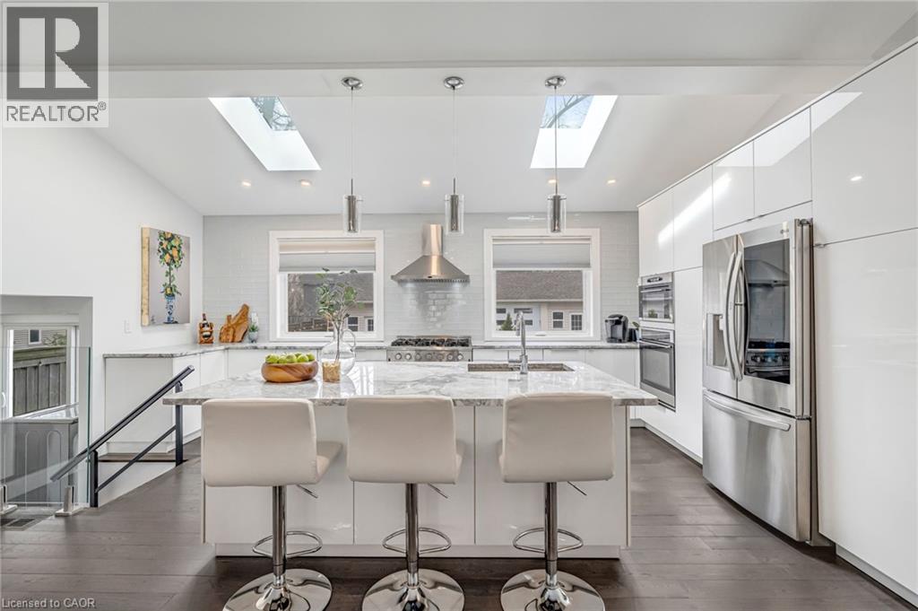Contemporary kitchen featuring a large central island with seating, white high-gloss cabinetry, stainless steel appliances, and skylights - 2123 Deyncourt Drive, Burlington, ON - Indoor