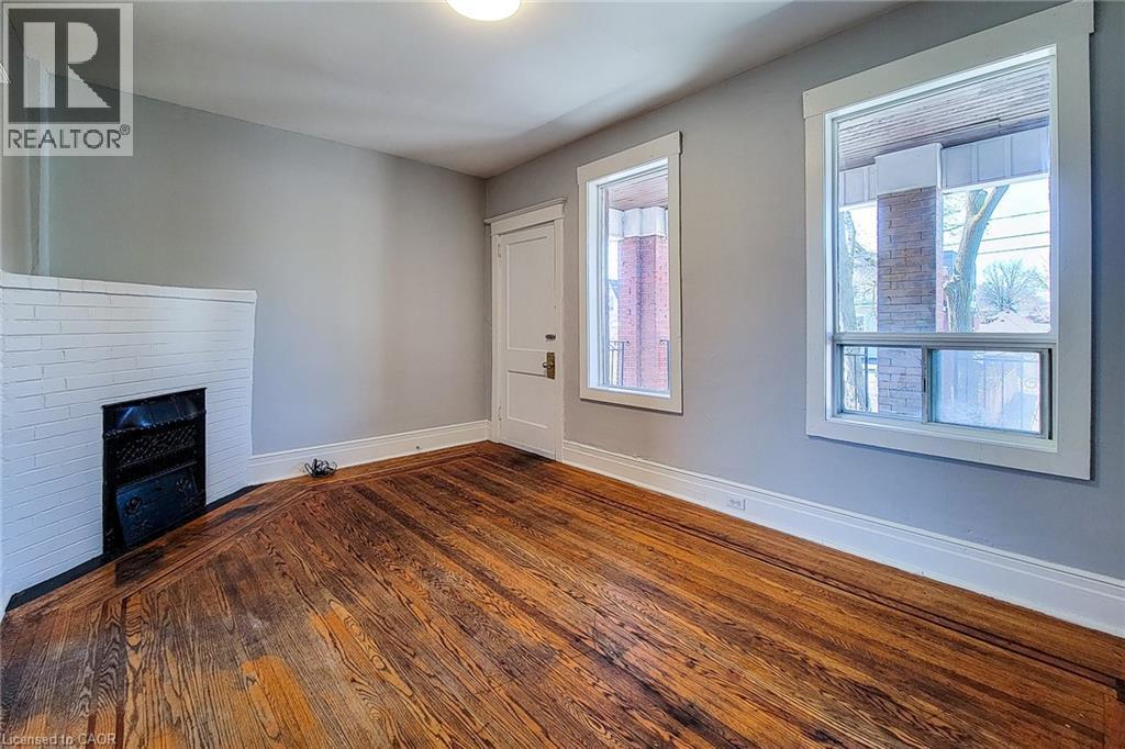Room featuring wood-finish flooring, a white-painted brick fireplace with an iron grate, and light grey walls - 254 Emerald Street N Unit# Upper, Hamilton, ON - Indoor Photo Showing Other Room