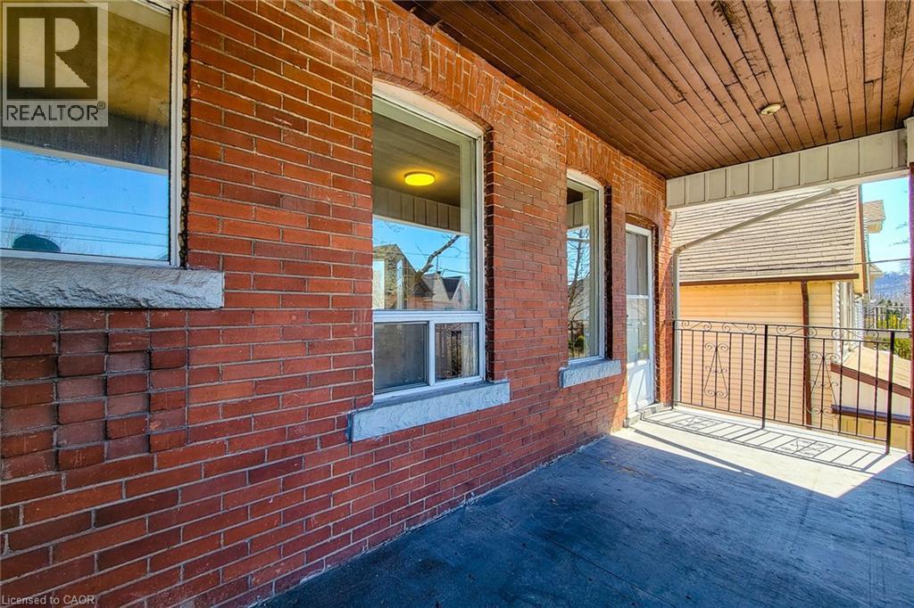 Brick exterior with white window trim and stone sills, featuring a covered porch with a wood plank ceiling, concrete flooring, and an ornate metal railing - 254 Emerald Street N Unit# Upper, Hamilton, ON - Outdoor With Exterior