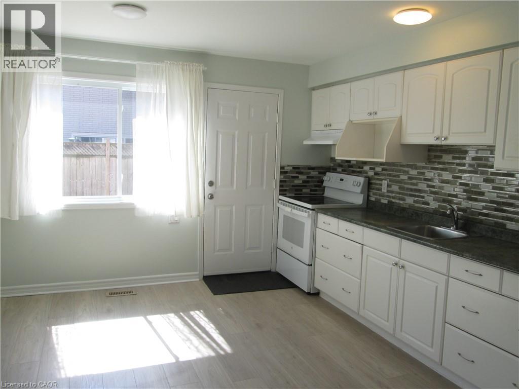 Kitchen featuring light wood-finish flooring, white cabinetry with silver hardware, a dark countertop, and a mosaic tile backsplash - 648 Francis Road, Burlington, ON - Indoor Photo Showing Kitchen