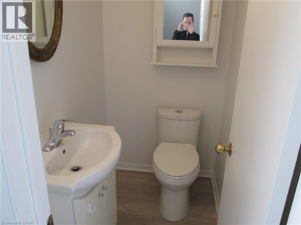 Compact powder room featuring a pedestal sink with chrome faucet, toilet, wall-mounted medicine cabinet, and wood-finish flooring - 648 Francis Road, Burlington, ON - Indoor Photo Showing Bathroom