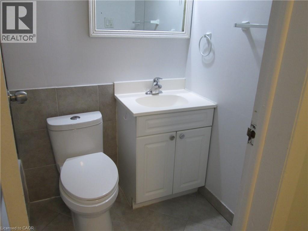 Bathroom featuring a white toilet, white vanity with integrated sink, chrome faucet, and a wall-mounted mirror - 648 Francis Road, Burlington, ON - Indoor Photo Showing Bathroom