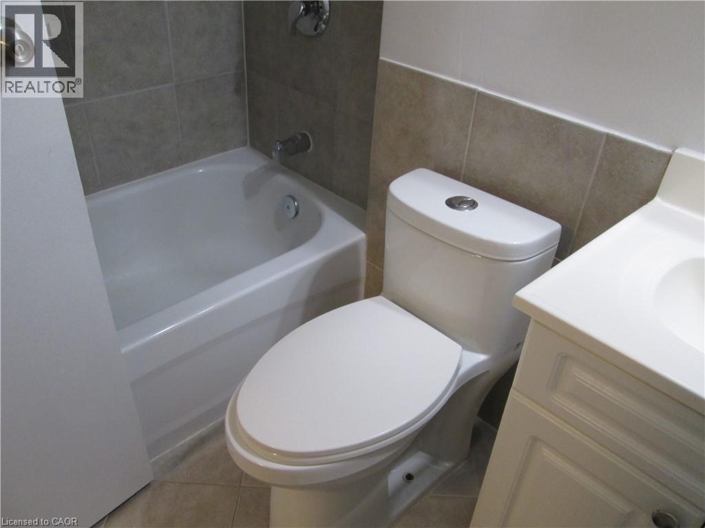 Bathroom featuring a white bathtub, tiled shower surround, commode with top-mounted flush button, and a white vanity with integrated sink - 648 Francis Road, Burlington, ON - Indoor Photo Showing Bathroom
