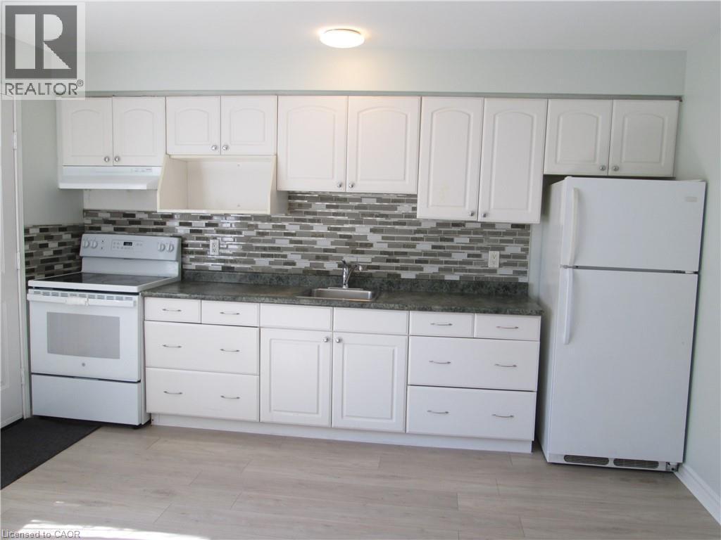 Kitchen featuring white cabinetry, a mosaic tile backsplash, dark-toned countertops, wood-finish flooring, and white appliances - 648 Francis Road, Burlington, ON - Indoor Photo Showing Kitchen