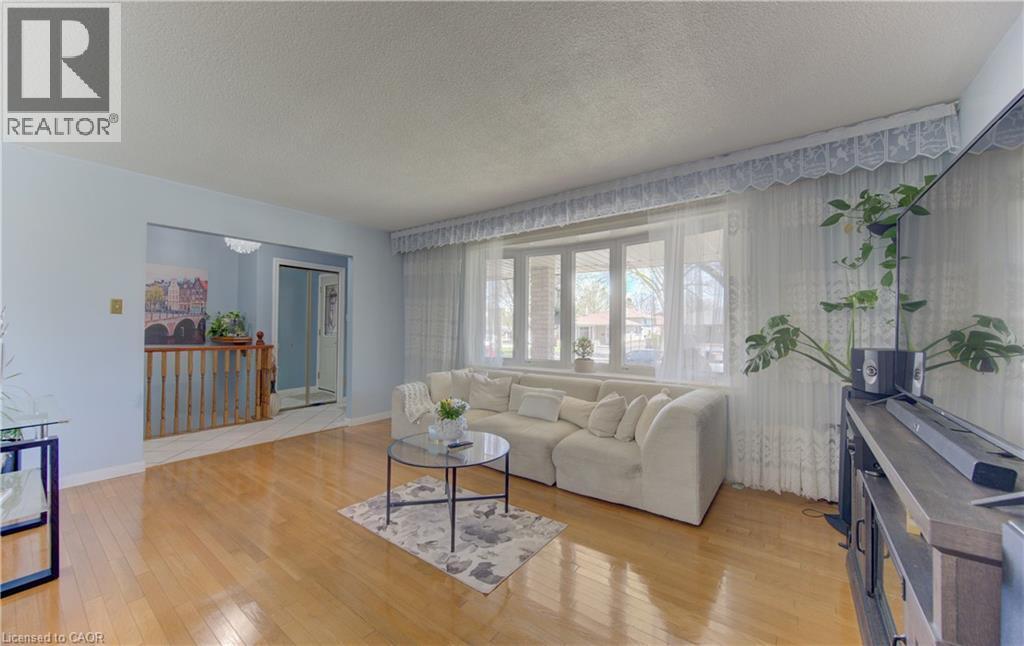 Bright living area featuring wood-finish flooring, a large bay window, light blue painted walls, and a decorative ceiling fixture visible in the adjacent hallway - 170 Martinglen Crescent, Kitchener, ON - Indoor Photo Showing Living Room