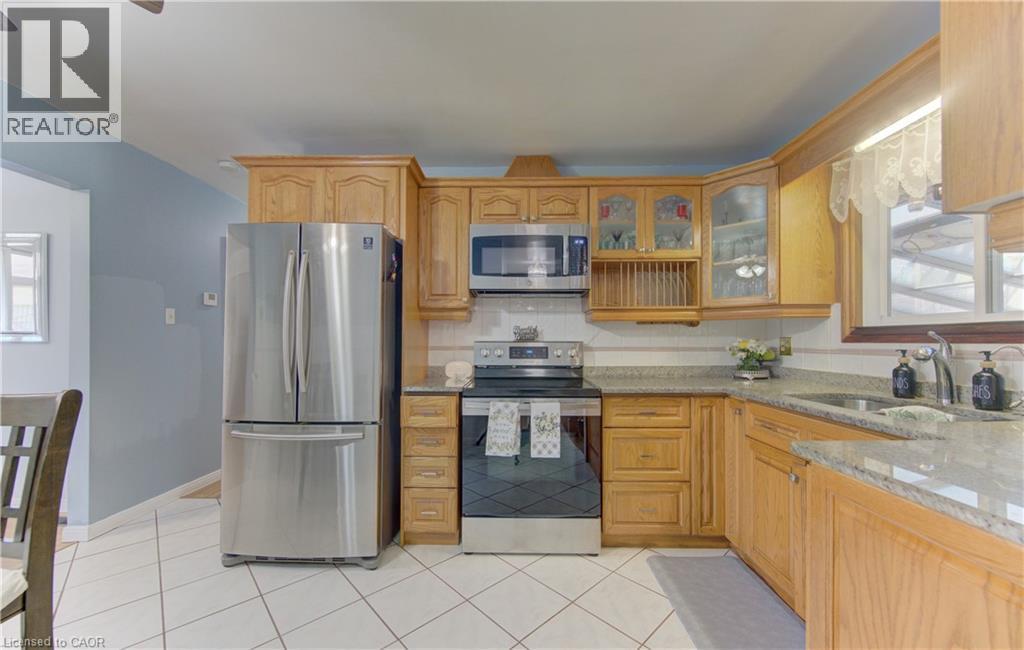 Kitchen featuring wood cabinetry, stainless steel appliances, white tile flooring, granite-look countertops, and a tile backsplash - 170 Martinglen Crescent, Kitchener, ON - Indoor Photo Showing Kitchen With Double Sink