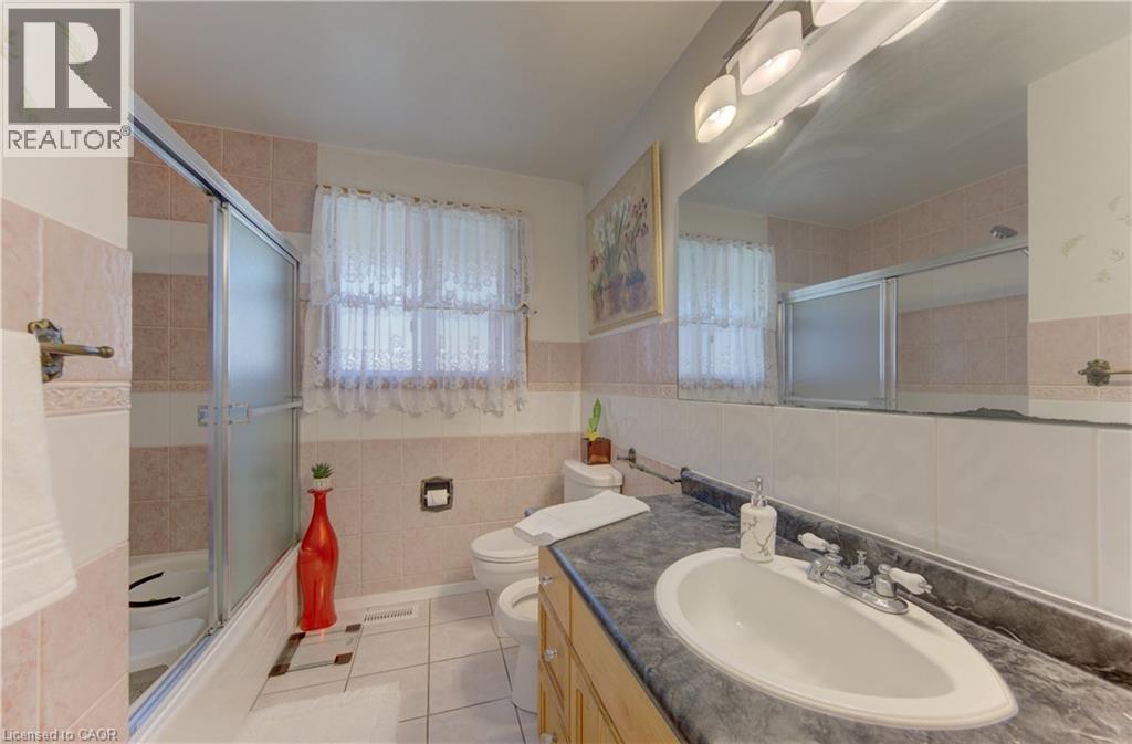 Bathroom featuring a shower enclosure with sliding frosted glass doors, a window with lace curtains, and a vanity with an integrated sink and dark countertop - 170 Martinglen Crescent, Kitchener, ON - Indoor Photo Showing Bathroom
