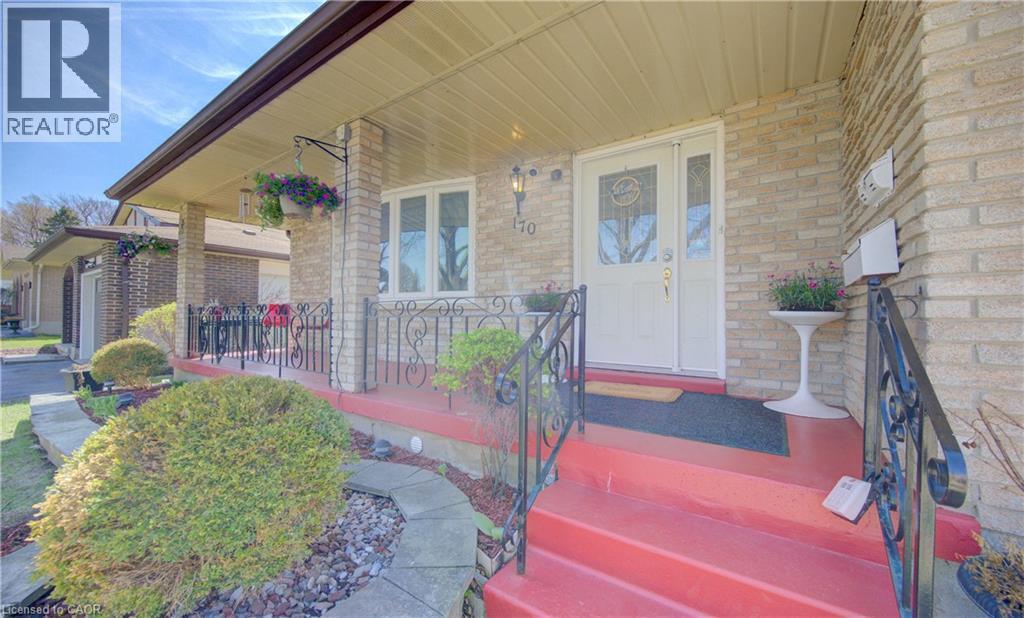 Brick exterior featuring a covered porch with a red-painted concrete surface, decorative wrought iron railing, and a white entrance door with sidelights - 170 Martinglen Crescent, Kitchener, ON - Outdoor