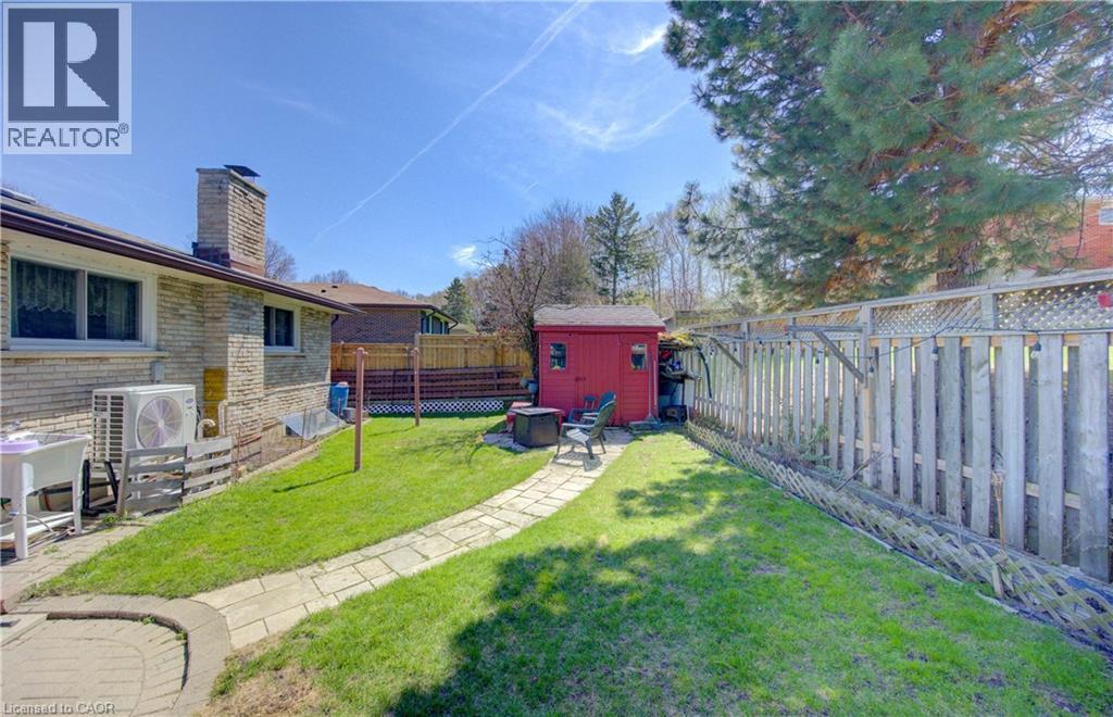 Expansive backyard featuring a manicured lawn, a stone paver pathway, a red storage shed, and a wooden privacy fence - 170 Martinglen Crescent, Kitchener, ON - Outdoor