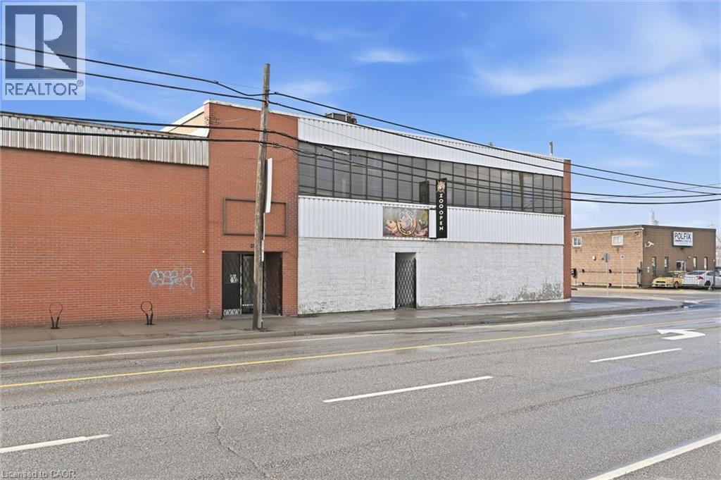 Commercial building featuring a brick facade, white siding, and a prominent storefront with large windows - 869 Barton Street E, Hamilton, ON