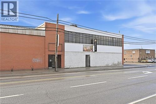 Commercial building featuring a brick facade, white siding, and a prominent storefront with large windows - 869 Barton Street E, Hamilton, ON 