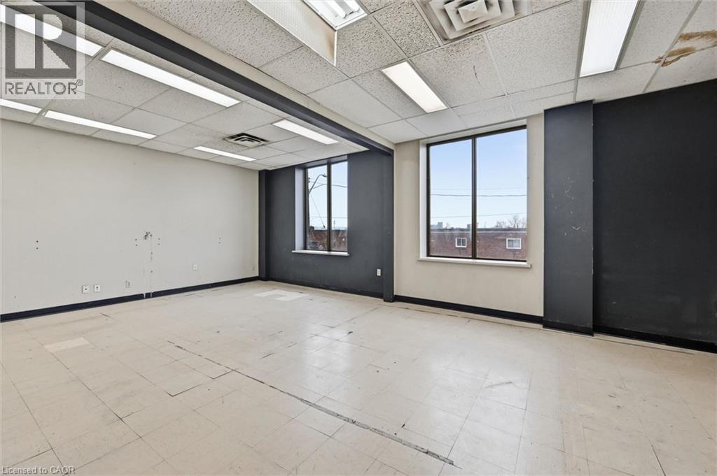 Spacious commercial interior featuring two large windows, drop ceiling with integrated fluorescent lighting, and a neutral-toned tile floor - 869 Barton Street E, Hamilton, ON