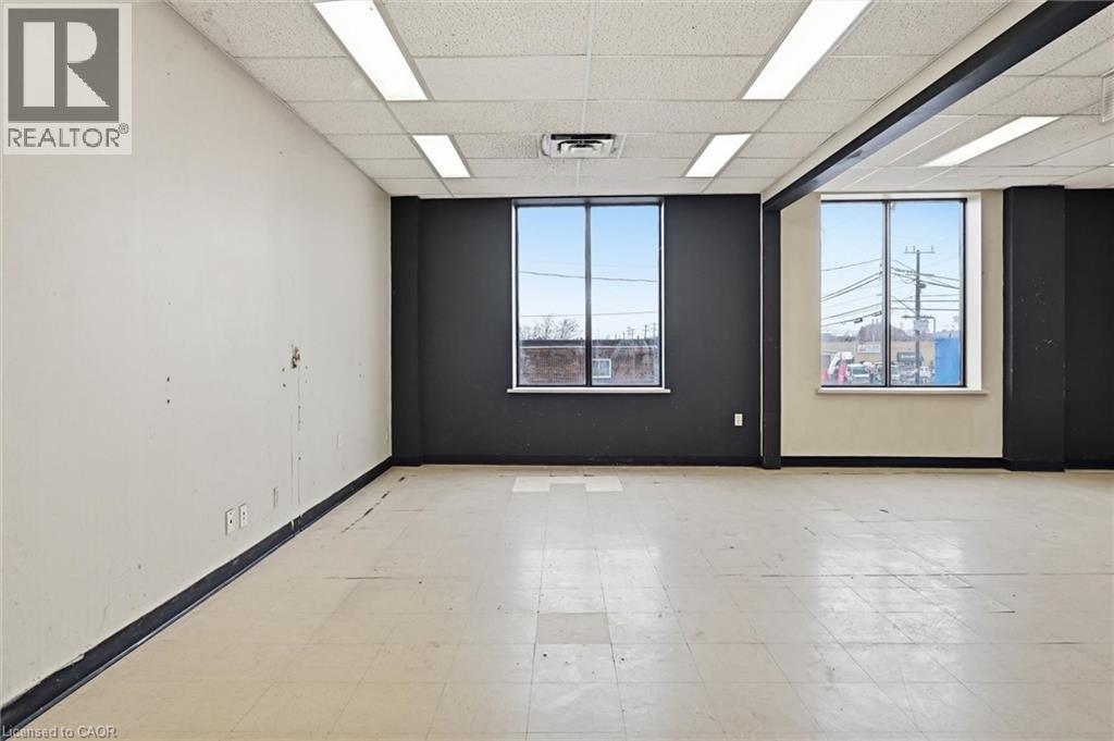 Spacious room featuring multiple large windows, recessed ceiling lighting, a suspended acoustic ceiling, and light-toned tile flooring - 869 Barton Street E, Hamilton, ON