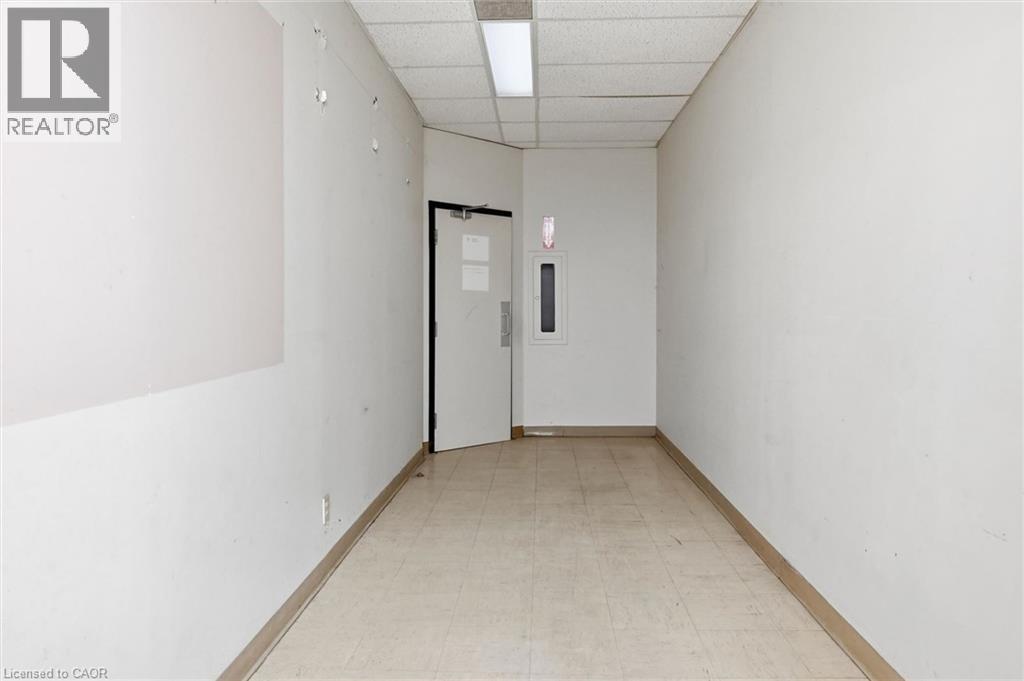 Corridor featuring light-toned square floor tiling, white painted walls, and a dropped ceiling with recessed fluorescent lighting - 869 Barton Street E, Hamilton, ON
