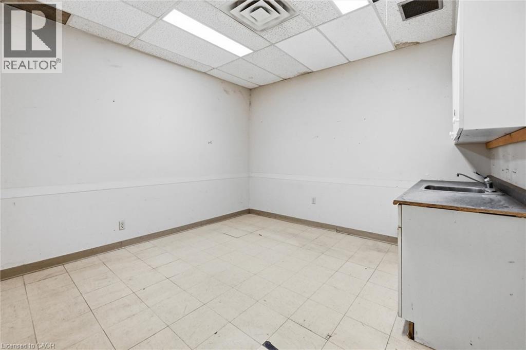 Compact utility area featuring a sink with a single-handle faucet, white cabinetry, and a drop ceiling with recessed lighting - 869 Barton Street E, Hamilton, ON