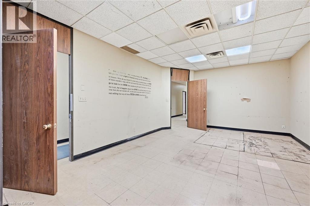 Spacious room featuring a drop ceiling with integrated lighting and air vents, wood-finish doors, and a tiled floor - 869 Barton Street E, Hamilton, ON