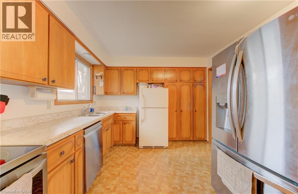 Kitchen featuring abundant wood cabinetry, light-toned countertops, a stainless steel dishwasher, and a stainless steel refrigerator - 98 Shea Crescent, Kitchener, ON - Indoor Photo Showing Kitchen